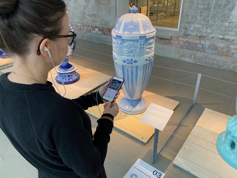 Person håller i mobiltelefon och skannar en QR-kod på marken på Rörstrand museum.